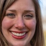 Close-up portrait of a smiling woman with bright eyes and red lips in natural light.